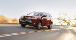 A red 2018 Toyota Highlander Hybrid driving down a sunny highway.