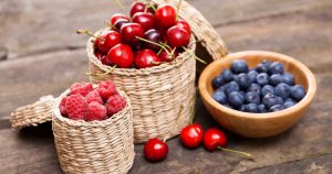 Three small baskets of berries (raspberries, cherries and blueberries) on a wooden table.
