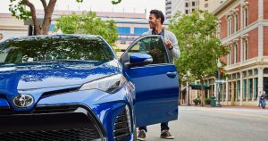 A blue 2019 Toyota Corolla parked on the side of a downtown street.