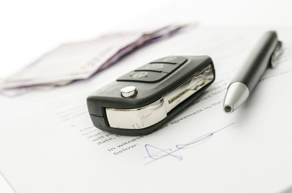 Close-up view of a car key fob, a pen and signature on paper