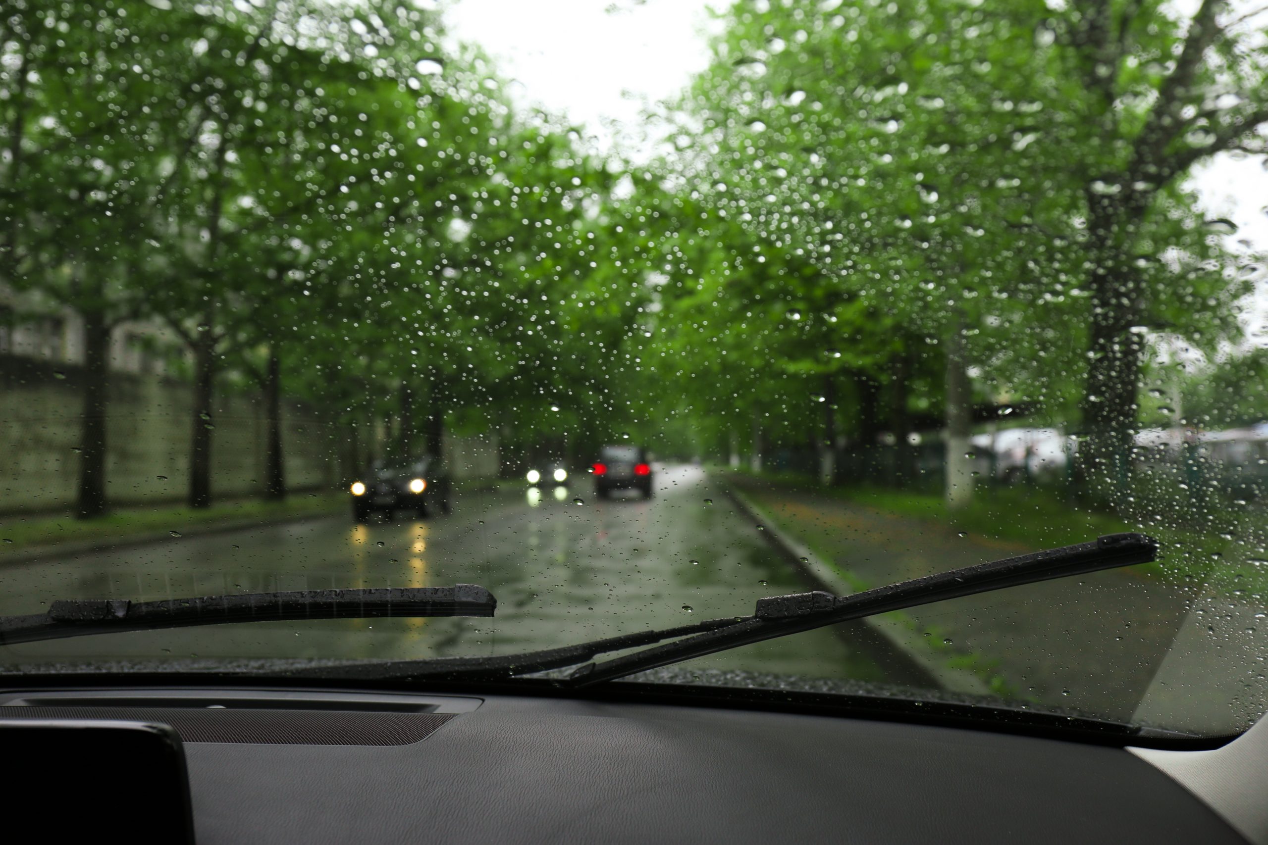 Interior of vehicle with active windshield wipers during light rain on the road