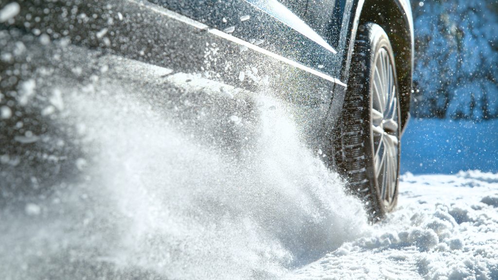 A close up of a car's wheels kicking up snow as it drives quickly.