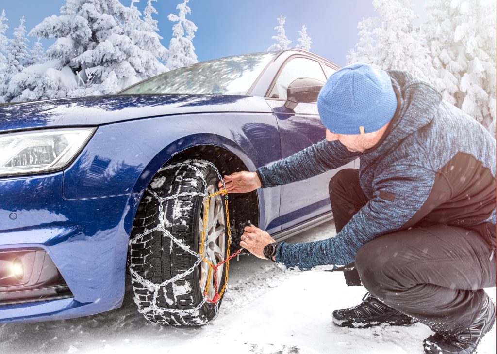 Man putting chains on vehicle's front tire.