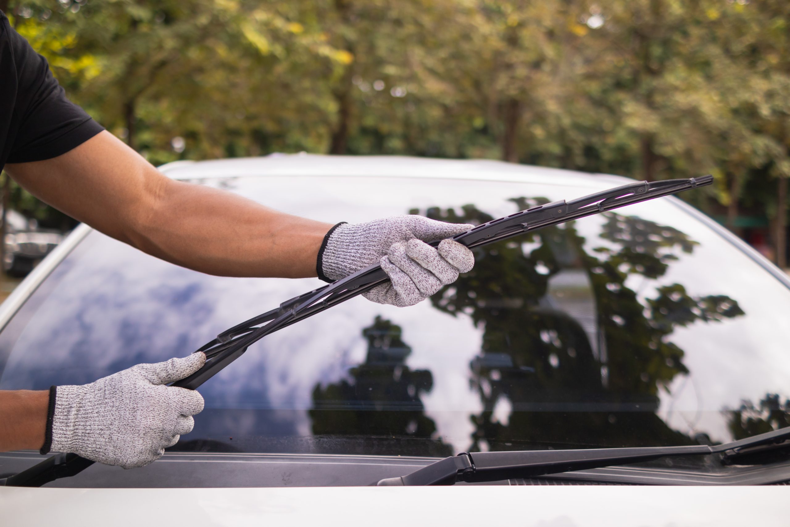 A man with gloves replacing a vehicle's windshield wipers.
