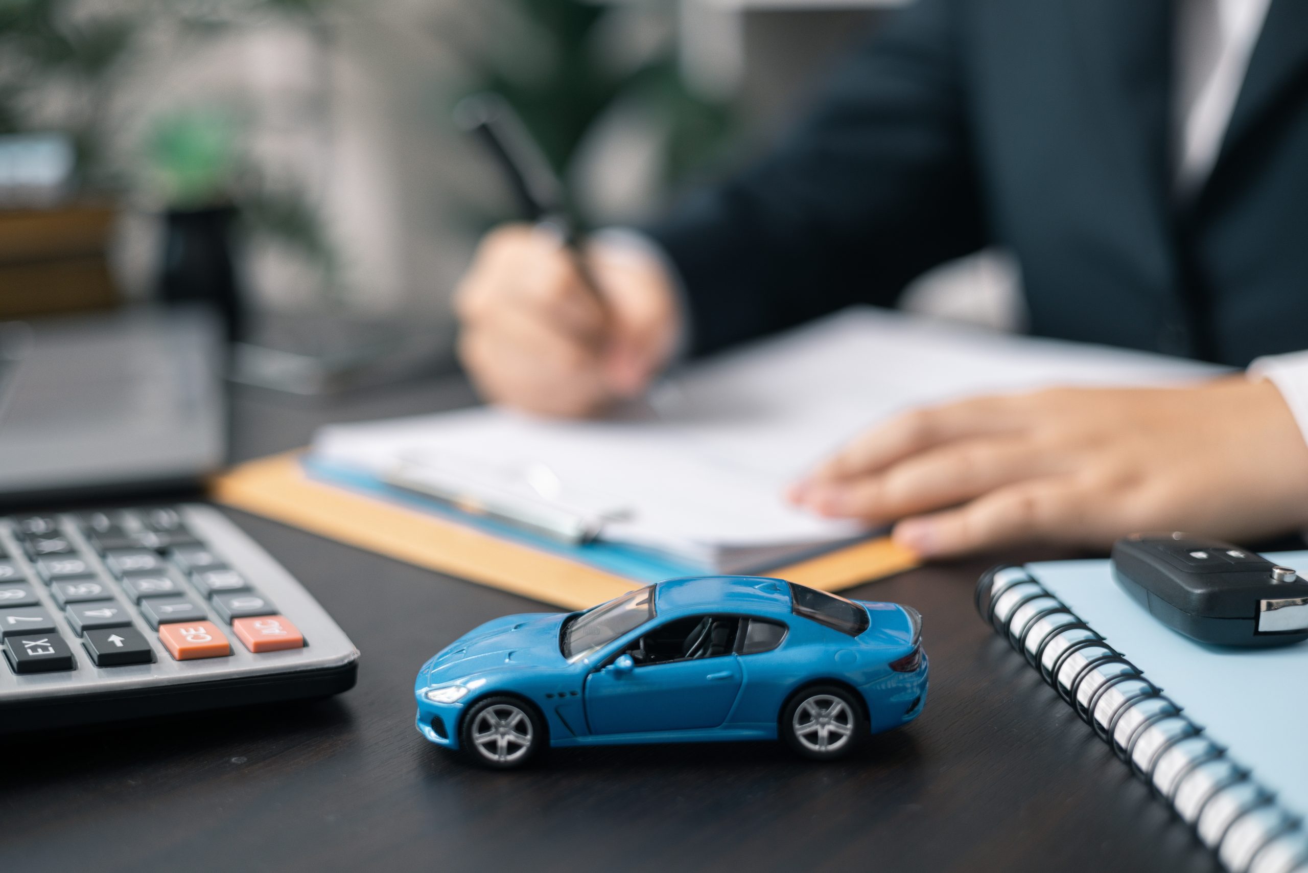 Man's hands signing document with a toy car on the desk.