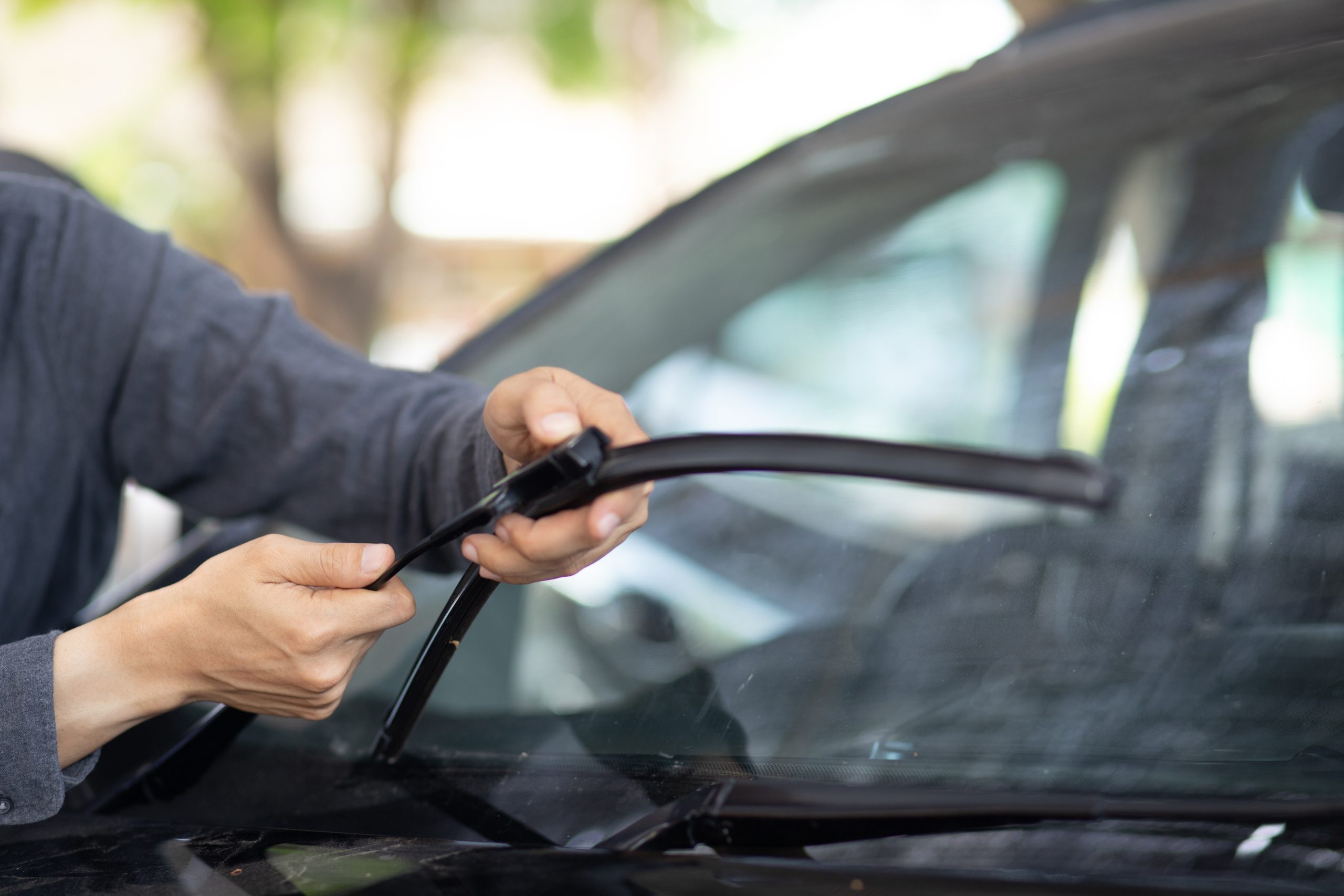A technician's hands replacing windshield wipers.
