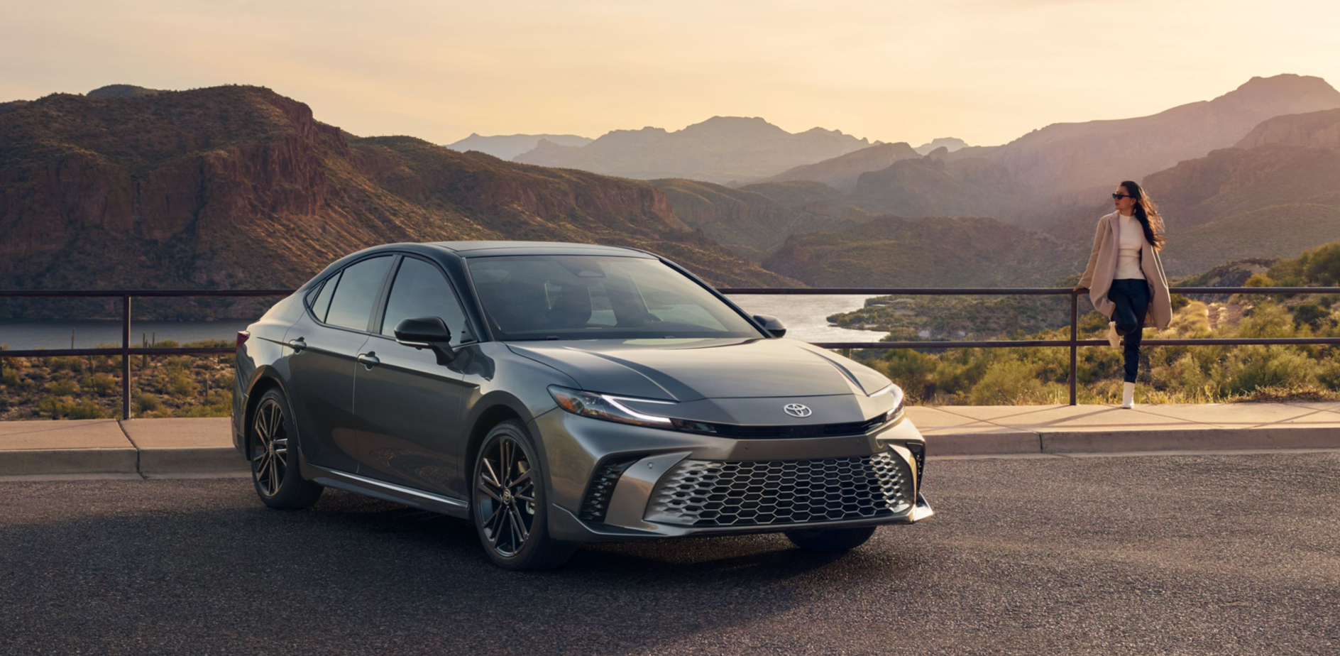 A gray 2025 Toyota Camry parked at an overlook over a mountain range with a woman nearby.