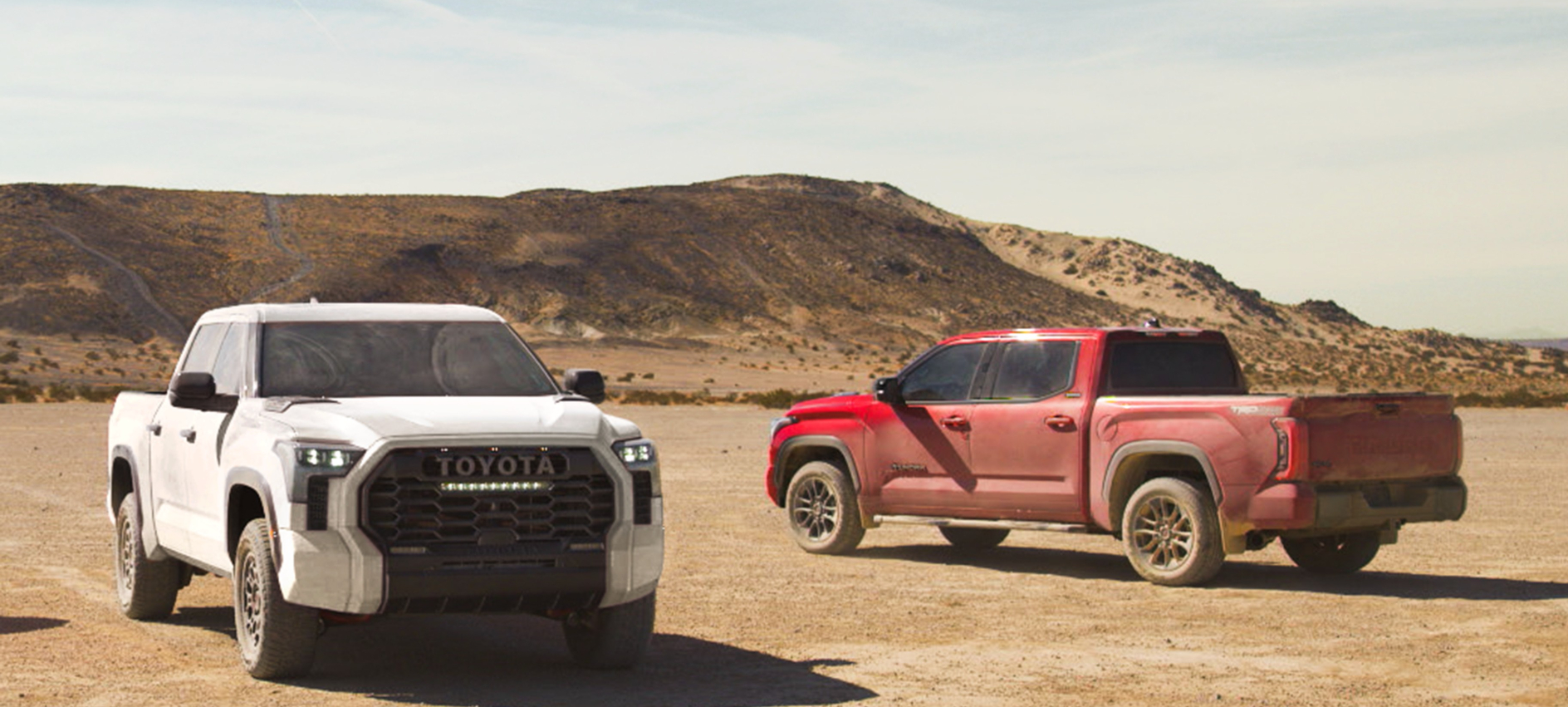 A red and white 2025 Toyota Tundra parked facing opposite directions in a desert.