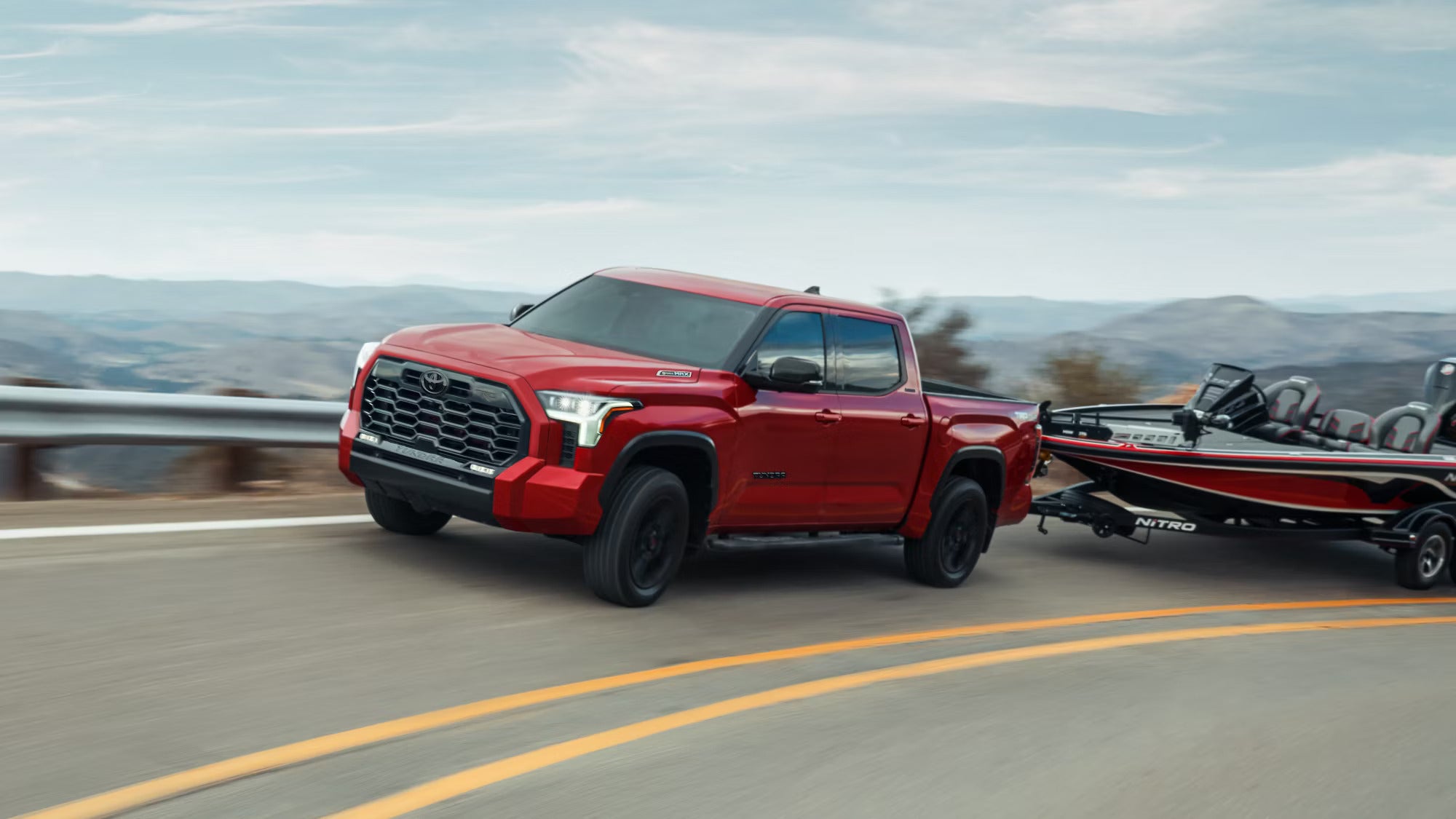 A red Toyota Tundra hauling a speedboat as it drives down the road.