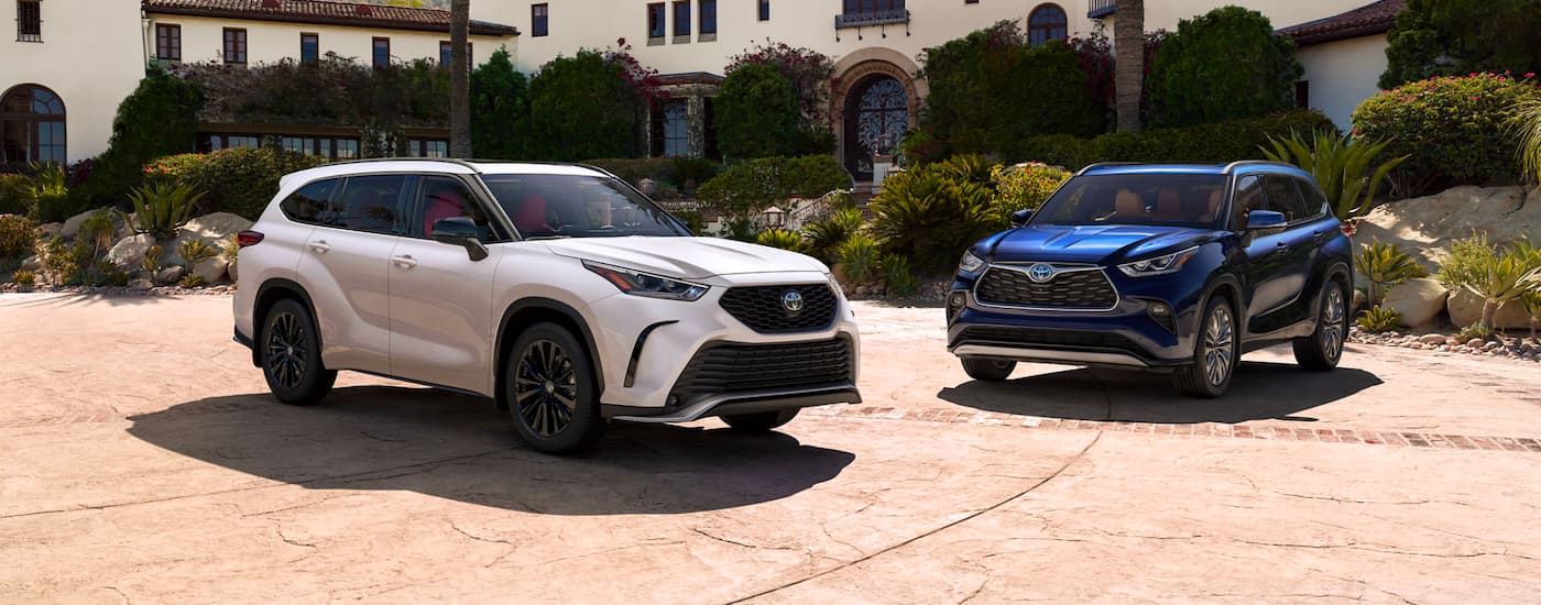 A white and a blue 2026 Toyota Highlander parked side by side in a driveway
